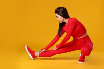 Wall Mural - Woman in sportswear exercising on orange background