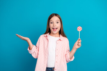 Wall Mural - Adorable young girl holding a colorful lollipop against a vibrant blue background