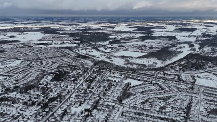 Wall Mural - Snow-covered city from above, under dramatic cloudy sky at sunset with farms in the background