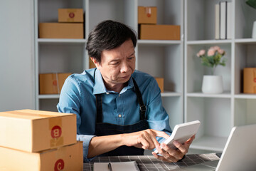 E-commerce entrepreneur analyzing data on a smartphone while seated at a desk surrounded by shipping boxes in a modern workspace.