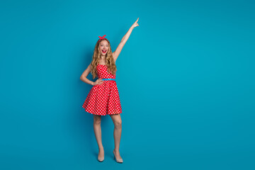 Wall Mural - Young woman with a pinup retro style pointing upward against a bright blue background