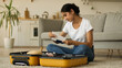 © Yuliia - Indian woman Arabian female ethnic girl Hindi lady at home indoors preparing for trip prepare for vacation travel with suitcase baggage luggage check passport documents plane airplane ticket honeymoon