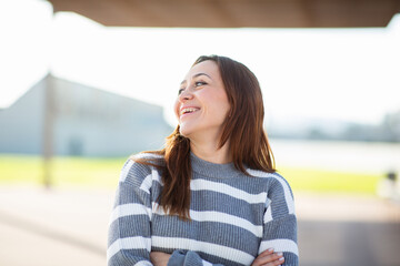 Smiling woman standing with arms crossed in urban park