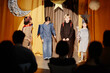© Seventyfour - Children dressed in costumes performing in school play on stage with moon and star decorations hanging in background, audience watching attentively from seats