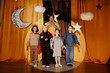 © Seventyfour - Children dressed in costumes standing on stage during school play with orange curtain background depicting night sky elements including moon and stars