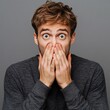 © Lal - Shocked youth hides mouth on gray backdrop.