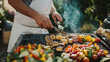 © mahamad - A chef grills vegetables and tofu at a vegan barbecue event, set in a garden for a summer gathering.