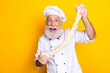 © deagreez - Smiling senior chef holding stretched dough on vibrant yellow background, highlighting culinary art and joyful cooking