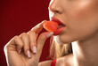 © Dimid - Beautiful young woman eating gummy candy in sugar on red background.