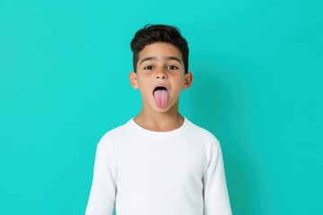 Wall Mural - A young boy is sticking his tongue out in a white shirt. The boy is smiling and he is having fun