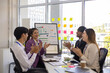 © Pattra - A group of people are gathered around a white board with a woman giving a presentation. Scene is positive and collaborative, as the group is clapping and smiling