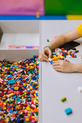 Wall Mural - A young teenage girl assembles a construction set from plastic parts and blocks with her hands.