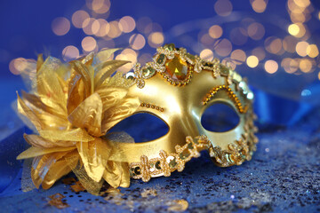 Beautiful carnival mask on blue glitter background against blurred lights, closeup. Bokeh effect