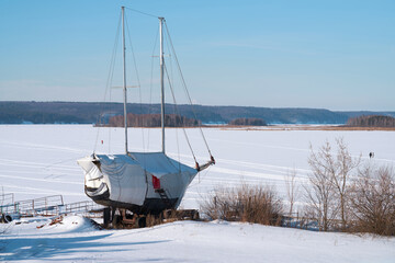 Wall Mural - Picturesque winter landscape. Winter parking of a sailing yacht on the shore of a frozen bay against the background of ice under snow.