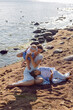 © saulich84 - A happy mother in a dress with two children aged seven and a baby are standing on a sandy beach by the sea in summer