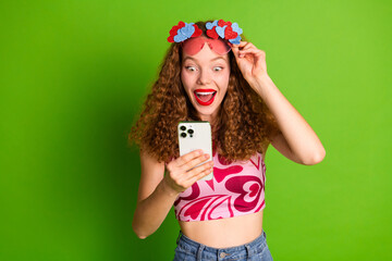 Wall Mural - Smiling young woman with red hair using smartphone against green background in festive outfit