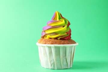 One delicious cupcake with colorful cream on green background, closeup