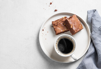 Wall Mural - Pieces of chocolate brownie with nuts on a plate with a cup of espresso coffee on a light background