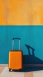 © Olena - travel orange blue, An orange suitcase stands against a vibrant blue and yellow wall, ready for an adventure, with a shadow adding depth to the scene.