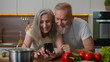 © Yuliia - Caucasian married couple bonding family old mature woman man read cooking recipe on mobile phone senior 50s husband wife talking hugging shopping online food order with smartphone together in kitchen