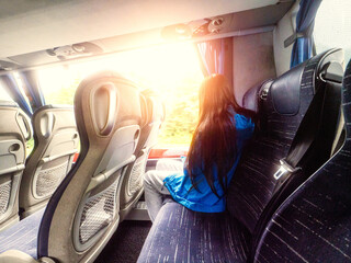 Young teenager girl in blue jacket sitting on back sit of a bus. Travel and tourism. Long journey. Light and airy look. Inside comfortable cabin on a trip.