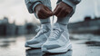 © Infinity Lens - Closeup of a man tying his gray and white sport shoes or sneakers, wearing a tracksuit, ready for jogging or walking outdoors in the summer. footwear lace tying, exercise healthy lifestyle for runner.