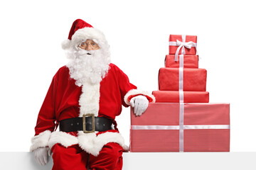 Wall Mural - Santa claus sitting on a banner with a pile of christmas presents