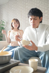 Wall Mural - A Japanese pregnant woman in her 20s, wearing a dress that shows her stomach, sits on a sofa in an apartment and her husband eats a hot pot dish.