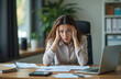 © Vadym - Businesswoman sits at home office desk overwhelmed by work. Headache, looks stressed. Papers, laptop on table. Working hard, feeling exhausted. Crisis deadline probably causing emotional stress.