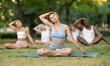 © JackF - Yoga female coach conduct rehearsal for multinational followers in park, leading of performing exercises, do fulfil padmasana, svastikasana. People practice sport during yoga workout in nature