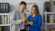 © Krakenimages.com - Man and woman discussing work in an office interior, focusing on a tablet, surrounded by shelves with files and documents in a business setting