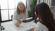 © Krakenimages.com - Two women discussing documents in an indoor office setting, showcasing a professional workplace atmosphere with business attire, computer equipment, and natural lighting.