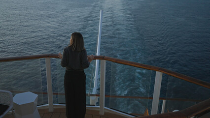 Young woman standing on a cruise ship deck enjoying a scenic ocean view under clear blue skies with a hint of exploration and adventure in the air