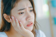 © MVProductions - Expression worry asian young woman hand touching pustule around the chin and mouth, allergic when wear mask, makeup, show squeezing pimple spot from face. Beauty care, skin problem by acne treatment