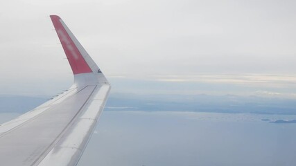 Wall Mural - view through plane window from inside airplane cabin while climbing flying over the sky with airplane wing winglet and fluffy cloud outside