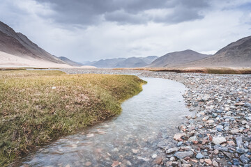 Wall Mural - Mountain river flows in the valley in the highlands of Tien Shan in Pamir in Tajikistan, panoramic landscape for background in high mountains with rocks, snow and glaciers