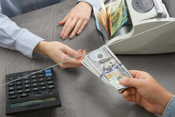 Cashier giving dollar banknotes to client at table in money exchange, closeup