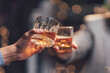 © Kritdanai - Toasting the Good Times: Two hands clink glasses filled with amber liquid, creating a warm and inviting atmosphere. The bokeh background suggests a festive gathering.