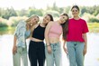 © Довидович Михаил - Four young women, dressed in casual summer clothes, stand together by a lake, enjoying each other's company