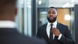 © Attasit - African ethnicity businessman adjusting his tie in front of a mirror before entering a corporate meeting, exuding confidence and professionalism