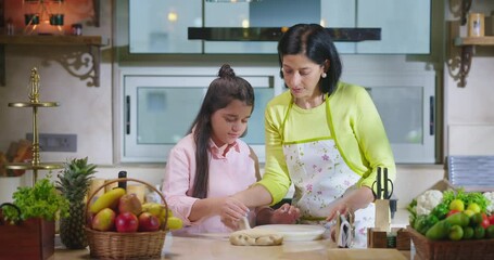 Indian happy woman lady with cute teen age cute girl rolling raw flour dough learn cooking food indoor home smiling young mom teach to kid child baking cookies enjoy day indoor modern home kitchen