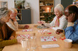 © AnnaStills - High angle shot of biracial senior company of friends sitting at wooden table and playing bingo together while in nursing home