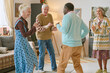 © AnnaStills - Wide shot of multiracial senior people dancing in center of living room in nursing home, they keeping rhythm and enjoying spare time