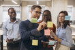 © anatoliycherkas - Group of diverse professionals brainstorming and collaborating on a project using sticky notes in a modern office setting