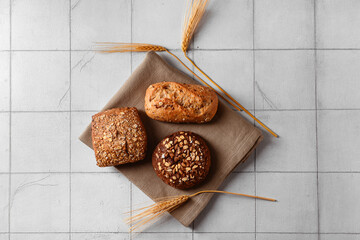 Canvas Print - Napkin with different delicious buns and wheat ears on grey tiled background