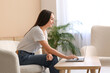 © Pixel-Shot - Young happy woman sitting on sofa and using laptop at coffee table in living room