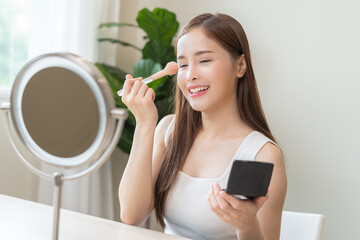 Wall Mural - Skin care beauty, applying make up concept, smile asian young woman, cute girl make up on face by brush blush powder on her cheek, looking at the mirror. Lady with cosmetic with fashion lifestyle