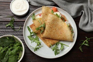 Wall Mural - Delicious crepes with salmon, cream cheese and arugula on wooden table, flat lay