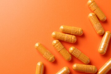 Wall Mural - Turmeric capsules on orange background, top view. Space for text