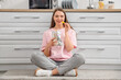© Pixel-Shot - Young woman with package of tasty nachos sitting on floor in kitchen